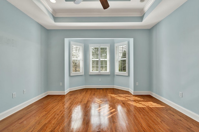 empty room featuring crown molding, a raised ceiling, baseboards, and hardwood / wood-style floors