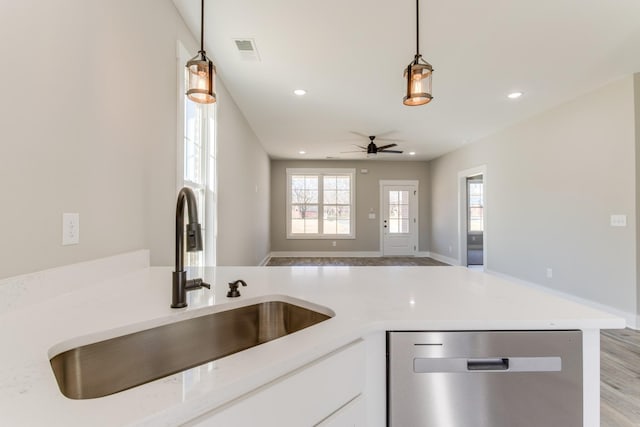 kitchen featuring visible vents, light countertops, stainless steel dishwasher, hanging light fixtures, and a sink