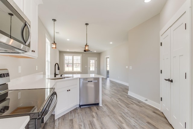 kitchen featuring light wood-style flooring, appliances with stainless steel finishes, a peninsula, white cabinets, and a sink