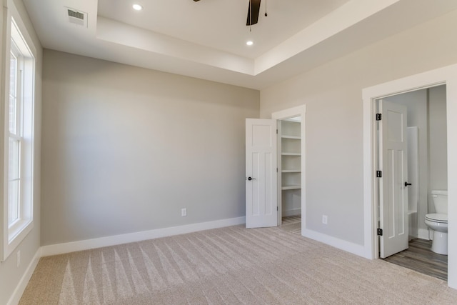 unfurnished bedroom featuring a tray ceiling, visible vents, baseboards, and carpet