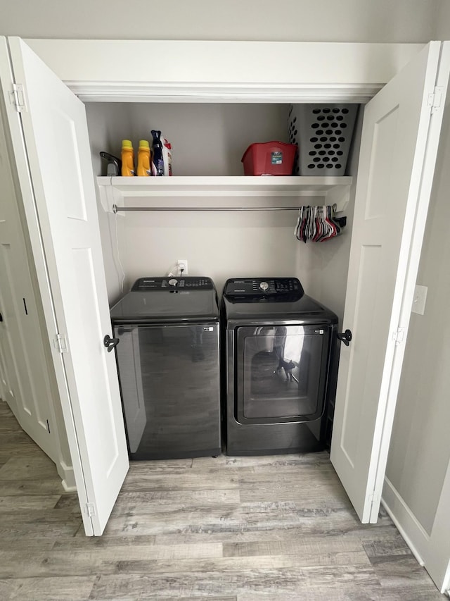 clothes washing area with baseboards, independent washer and dryer, laundry area, and light wood finished floors