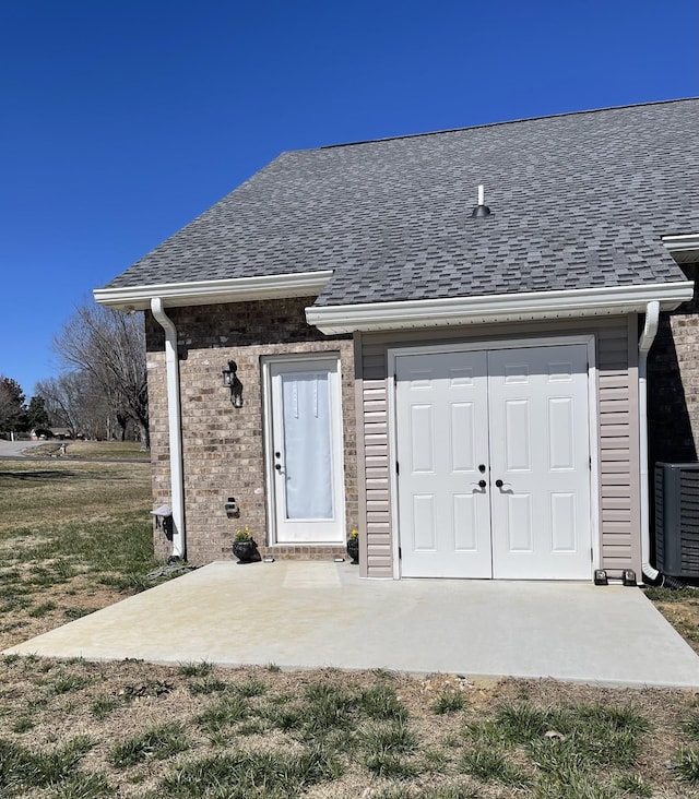 exterior space featuring brick siding, central AC, and roof with shingles