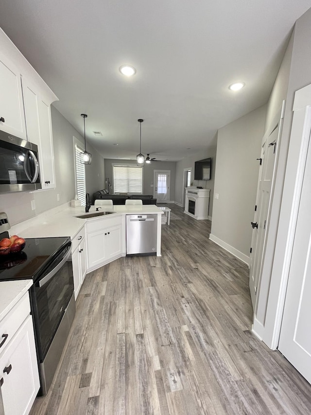 kitchen featuring light wood-type flooring, a sink, open floor plan, appliances with stainless steel finishes, and a peninsula