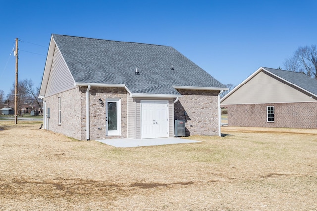 rear view of property with a patio, brick siding, roof with shingles, and a lawn