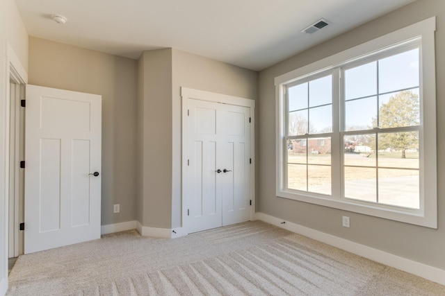 unfurnished bedroom featuring a closet, visible vents, light colored carpet, and baseboards