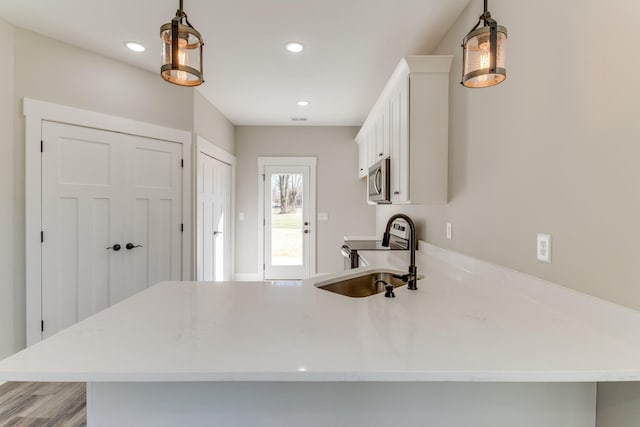 kitchen featuring light countertops, a peninsula, stainless steel appliances, white cabinetry, and a sink