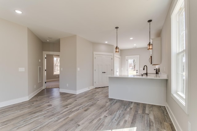 kitchen with baseboards, visible vents, light wood finished floors, a peninsula, and light countertops