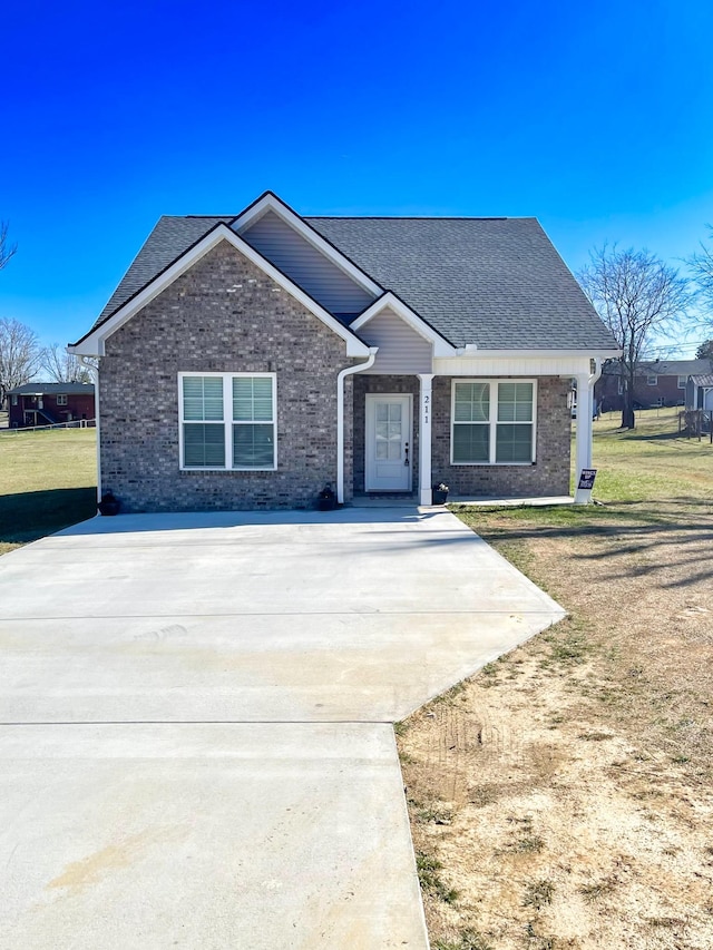 view of front of house featuring driveway, brick siding, a front lawn, and a shingled roof