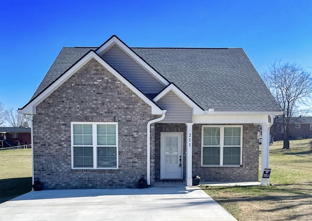 view of front of property featuring brick siding, a front lawn, and a shingled roof