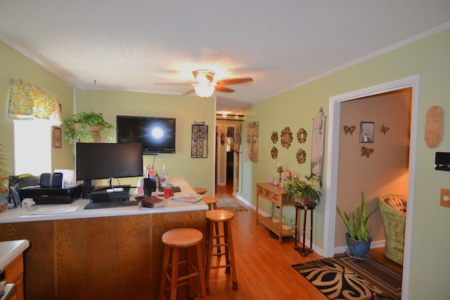 kitchen featuring a ceiling fan, baseboards, light wood-style floors, a textured ceiling, and a kitchen breakfast bar