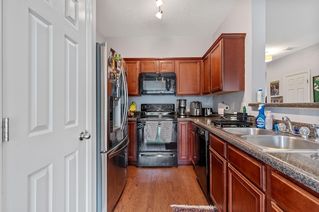 kitchen featuring visible vents, black appliances, a sink, light wood-style floors, and brown cabinetry