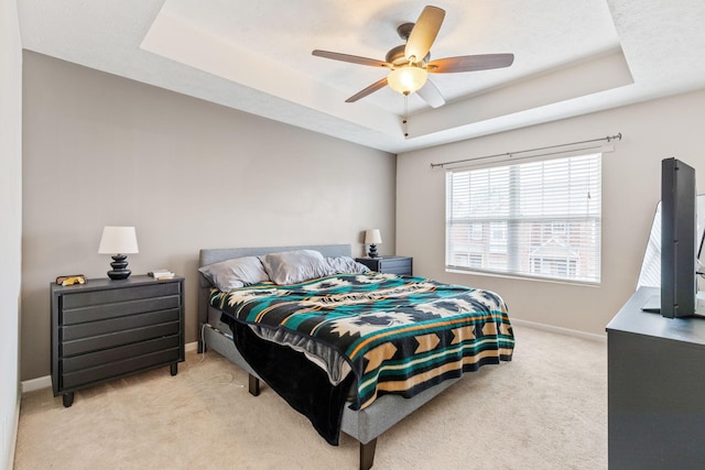 bedroom with baseboards, a raised ceiling, light colored carpet, and ceiling fan