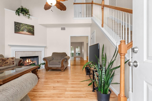 living room featuring visible vents, light wood-style flooring, ceiling fan, a fireplace, and a towering ceiling