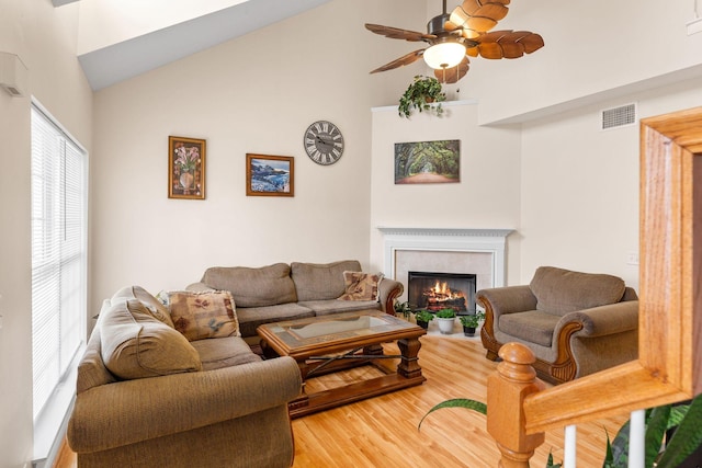 living room with light wood-type flooring, visible vents, high vaulted ceiling, ceiling fan, and a tile fireplace