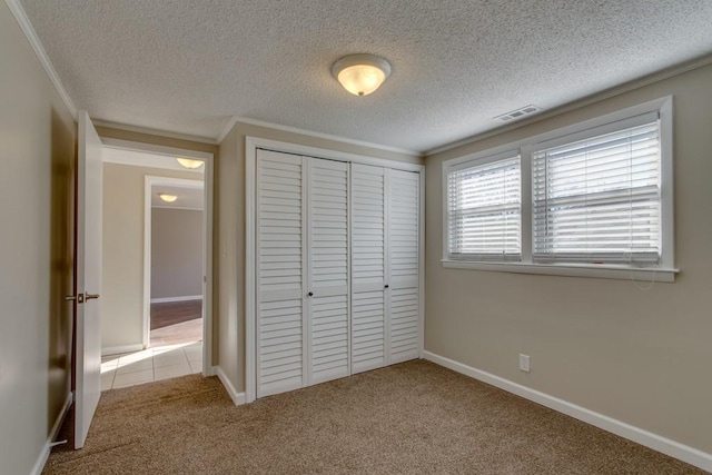 unfurnished bedroom featuring visible vents, crown molding, baseboards, carpet floors, and a closet