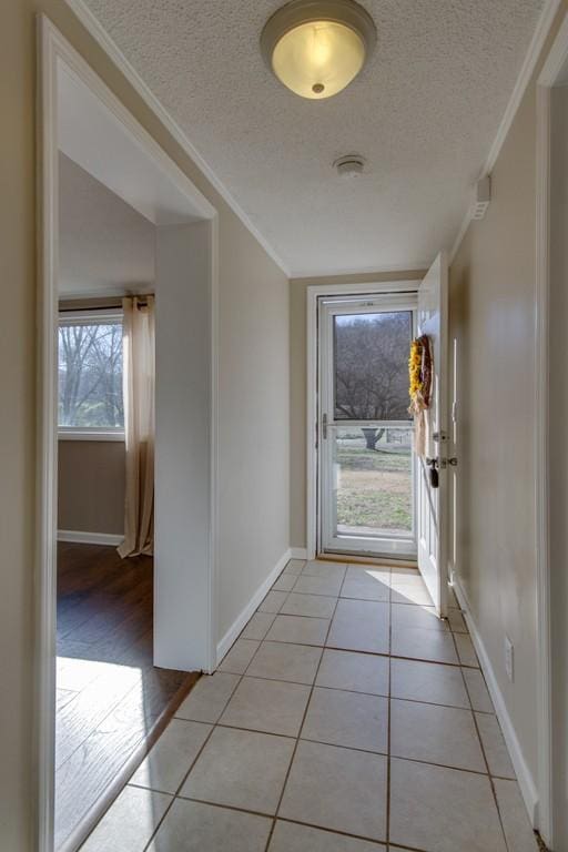 doorway with light tile patterned floors, baseboards, a textured ceiling, and crown molding