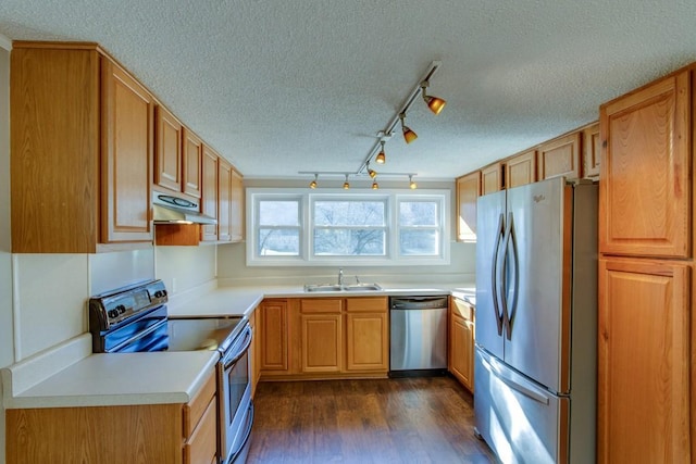 kitchen with dark wood finished floors, appliances with stainless steel finishes, exhaust hood, a textured ceiling, and a sink