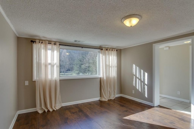 empty room with crown molding, wood finished floors, visible vents, and baseboards