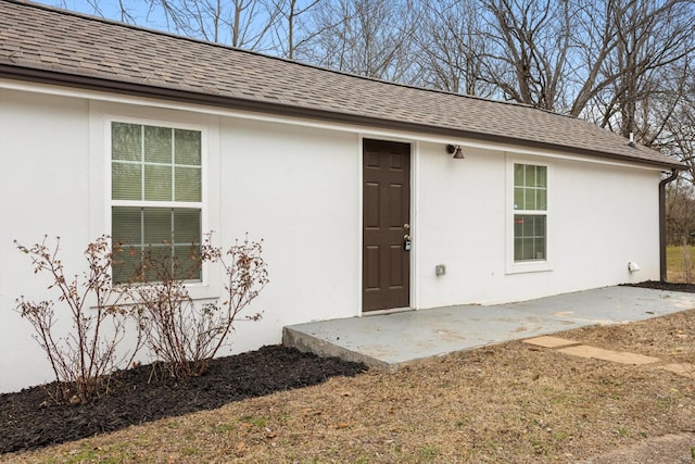 entrance to property with stucco siding, a patio, and roof with shingles