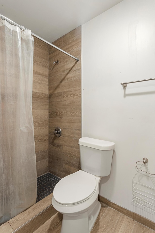 bathroom with baseboards, toilet, wood finished floors, and a tile shower