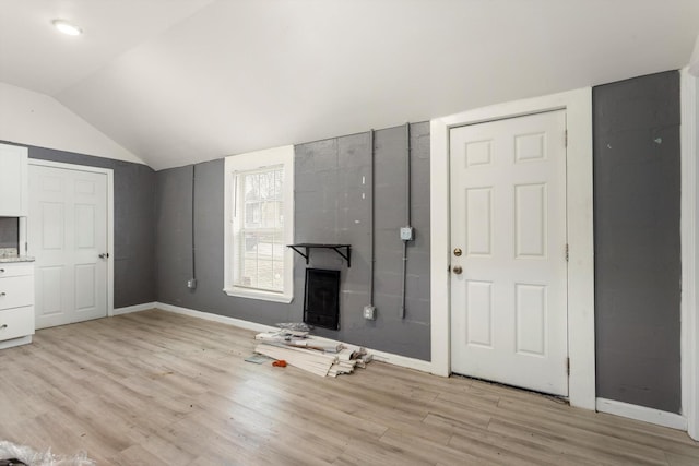 unfurnished living room with vaulted ceiling, baseboards, and light wood finished floors