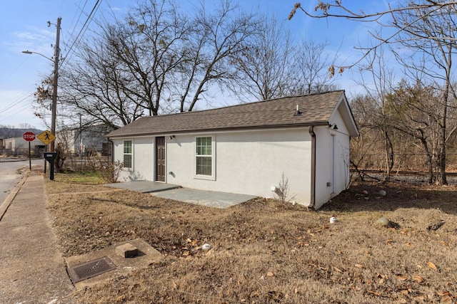 view of front of house with a patio area, roof with shingles, and stucco siding