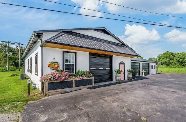 exterior space with a yard, stucco siding, a garage, central air condition unit, and metal roof