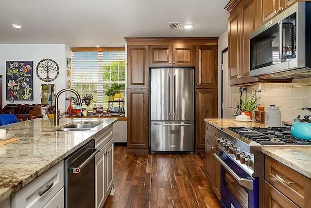 kitchen featuring light stone counters, visible vents, a sink, stainless steel appliances, and dark wood-type flooring