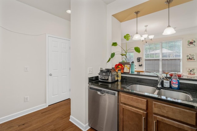 kitchen with pendant lighting, a sink, stainless steel dishwasher, wood finished floors, and dark stone counters