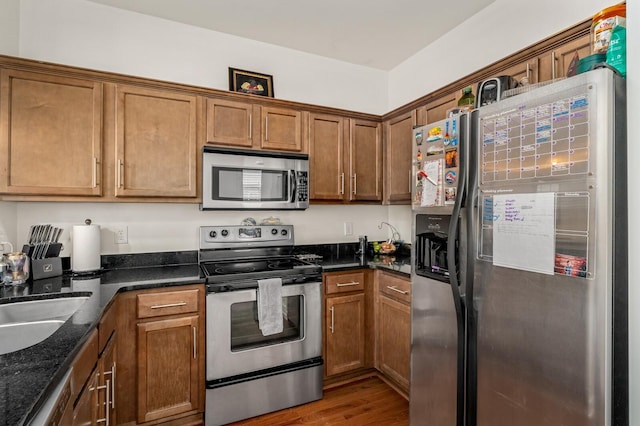 kitchen featuring dark stone counters, brown cabinets, appliances with stainless steel finishes, and wood finished floors