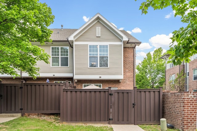 rear view of property with a gate, fence, brick siding, and roof with shingles