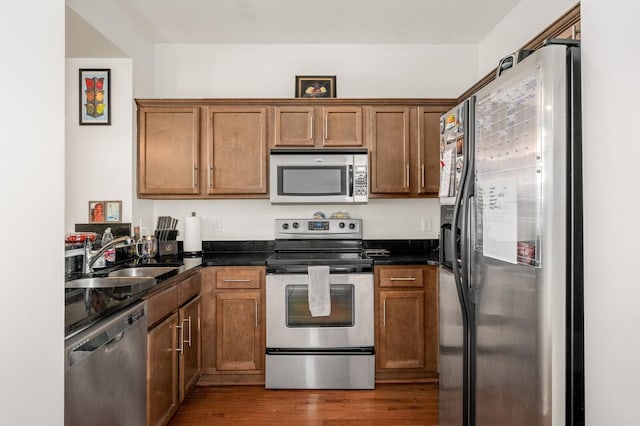 kitchen with a sink, brown cabinets, dark wood-style flooring, and stainless steel appliances