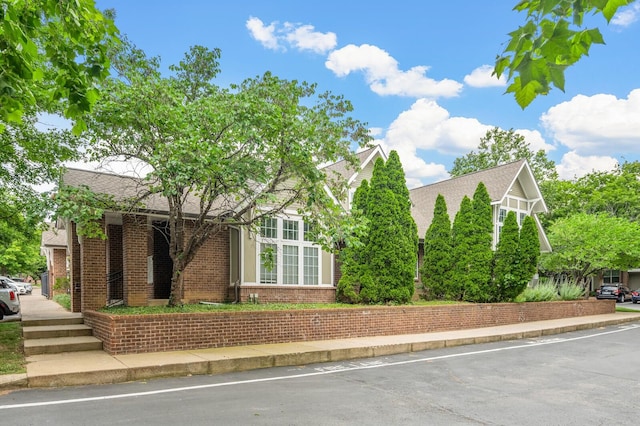 view of property hidden behind natural elements featuring brick siding and roof with shingles