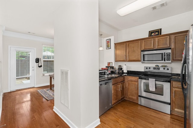 kitchen featuring light wood-style floors, stainless steel appliances, dark countertops, and visible vents