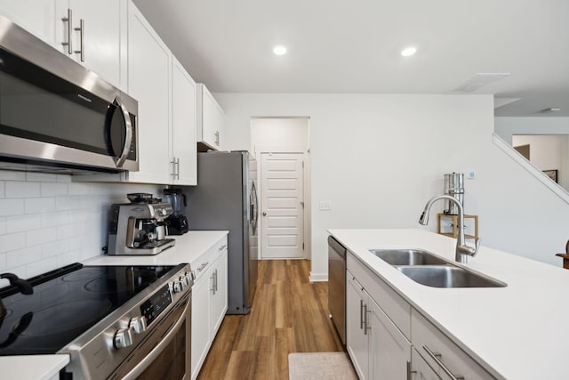 kitchen featuring a sink, backsplash, wood finished floors, appliances with stainless steel finishes, and light countertops