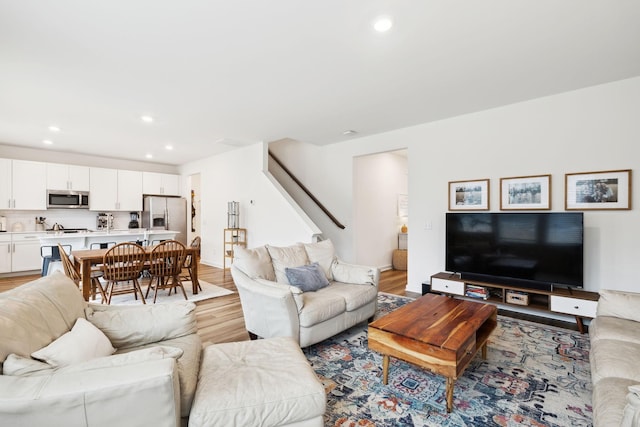 living room with recessed lighting, light wood-style flooring, stairs, and baseboards