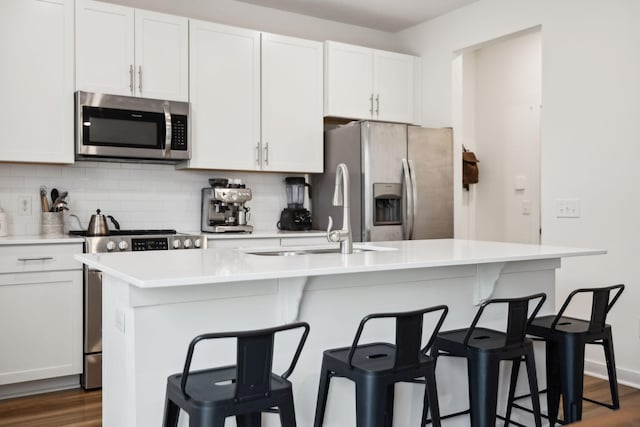 kitchen with an island with sink, a sink, dark wood-style floors, appliances with stainless steel finishes, and decorative backsplash