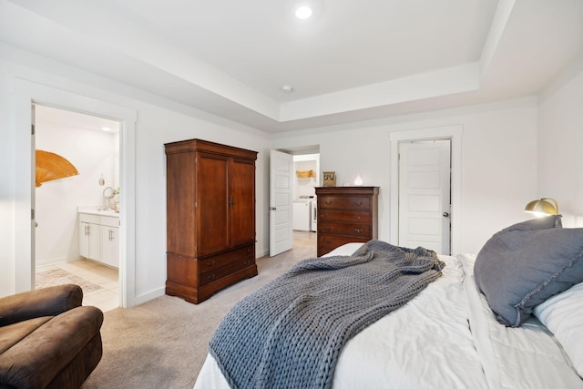 bedroom with baseboards, light carpet, washer / dryer, ensuite bathroom, and a raised ceiling