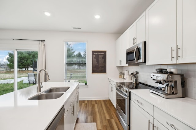 kitchen with a sink, wood finished floors, stainless steel appliances, light countertops, and decorative backsplash