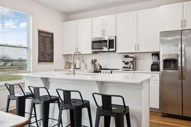 kitchen featuring stainless steel appliances, light countertops, light wood-style floors, white cabinetry, and tasteful backsplash