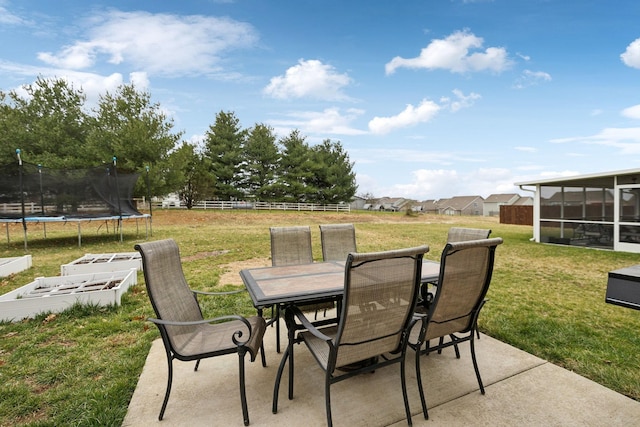 view of patio with outdoor dining area, a sunroom, a trampoline, and fence