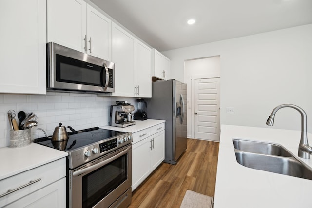 kitchen featuring backsplash, stainless steel appliances, wood finished floors, white cabinetry, and a sink