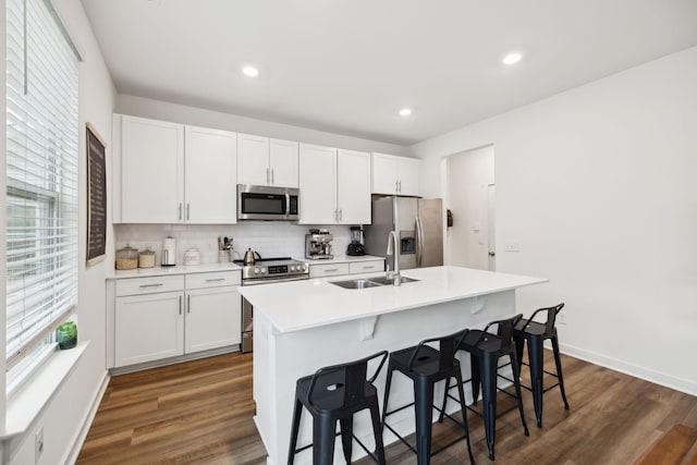 kitchen featuring an island with sink, a sink, dark wood-style floors, stainless steel appliances, and a breakfast bar area