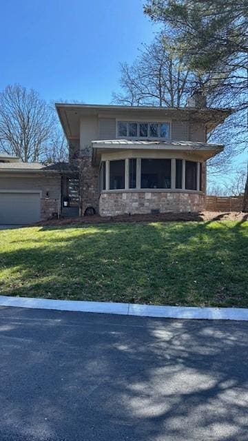 view of front of house with stone siding, an attached garage, a front lawn, and a sunroom