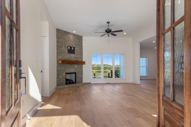 unfurnished living room featuring a stone fireplace, light wood-style flooring, baseboards, and ceiling fan