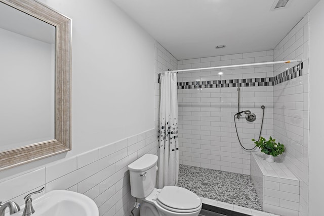 full bath with visible vents, tiled shower, a sink, tile walls, and toilet