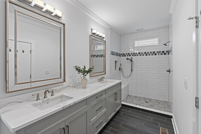 full bath with a tile shower, ornamental molding, double vanity, and a sink