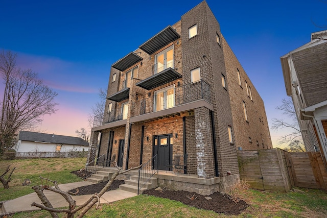 view of front of house with a balcony, a porch, brick siding, and fence