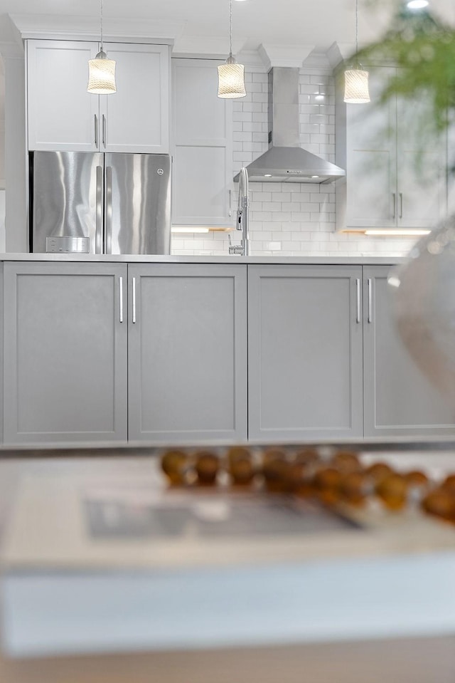 kitchen featuring light countertops, wall chimney range hood, freestanding refrigerator, and pendant lighting