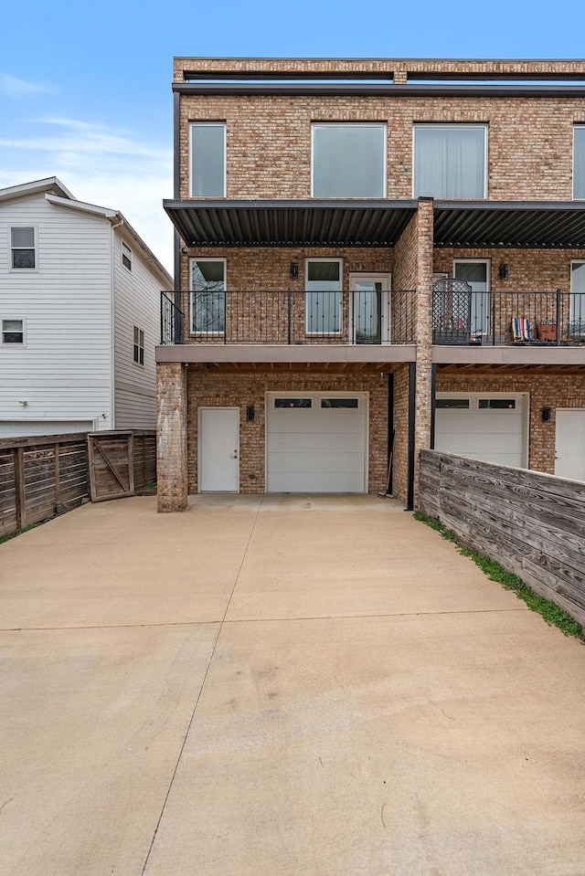 multi unit property featuring a balcony, fence, driveway, an attached garage, and brick siding